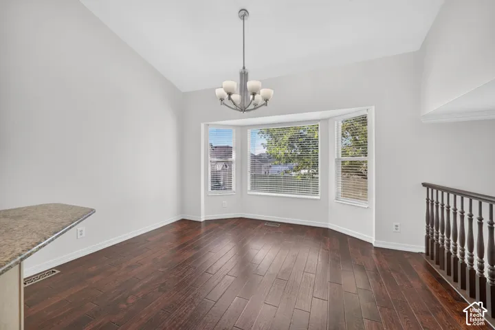 Vaulted ceiling with a chandelier, bay window with blinds, wood-finish flooring, and a stone-finish countertop