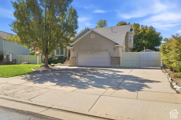 Stucco and stone exterior, attached garage, concrete driveway, mature trees, and privacy fencing