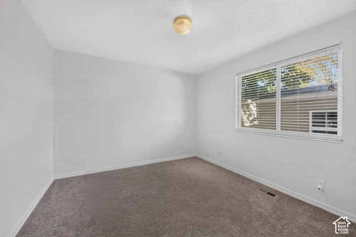 Neutral wall paint with textured carpeting and a rectangular window featuring horizontal blinds