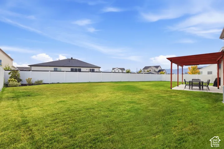 Expansive backyard featuring a lush lawn, white vinyl fencing, and a concrete patio with a wood pergola