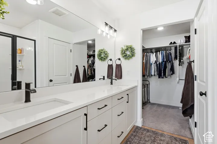 Dual undermount sinks with matte black faucets, an expansive vanity with shaker-style cabinetry, and a walk-in closet with built-in shelving