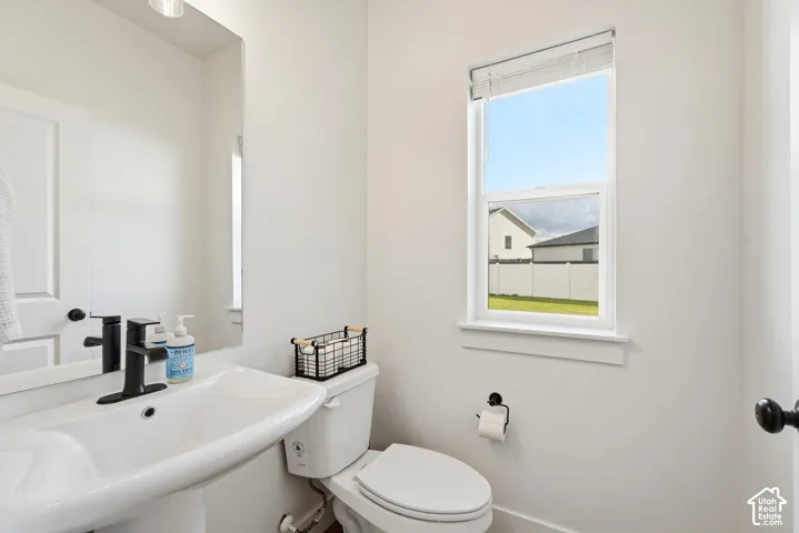Pedestal sink with a matte black faucet, wall-mounted mirror, and a single window