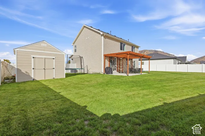 Expansive backyard featuring a manicured lawn, a detached storage shed, a pergola-covered patio, and a privacy fence