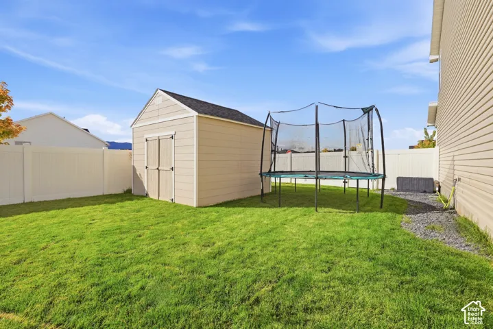 Expansive backyard featuring a storage shed with a shingle roof, green lawn, gravel path, and a privacy fence