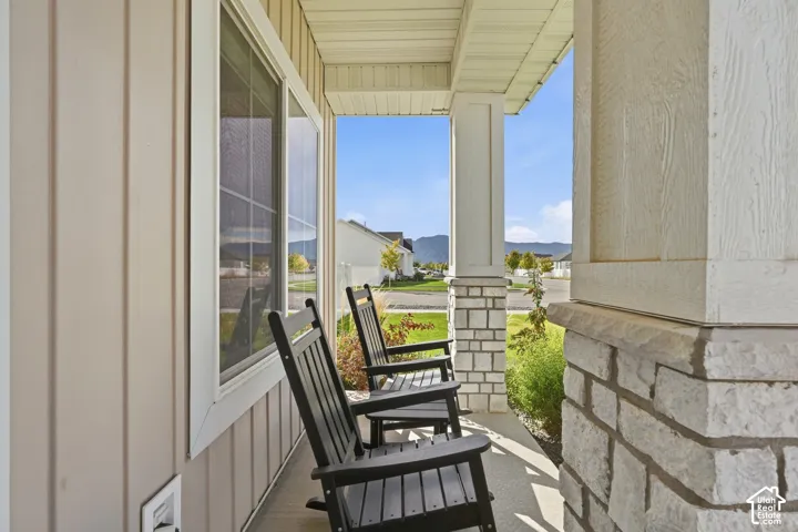 Covered front porch featuring textured stone columns, vertical panel siding, and a large window with white trim