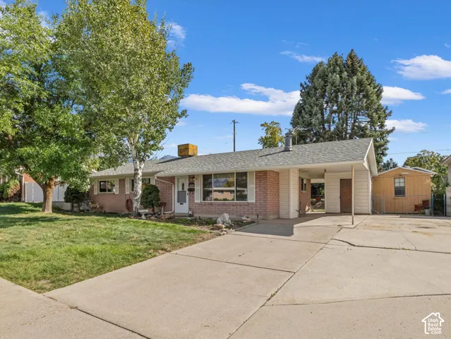 Brick facade, concrete driveway, attached carport, mature trees, and detached shed