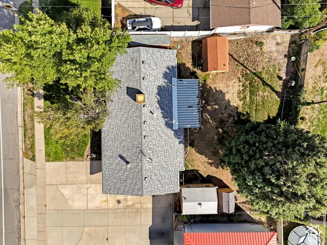 Asphalt shingle roof with a chimney, a covered patio structure, and mature trees