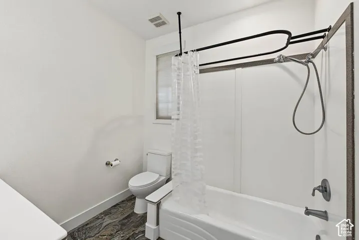Bathroom featuring a white bathtub, shower combination with a flexible showerhead, and dark wood-finish flooring
