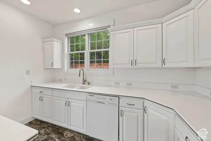White shaker-style cabinetry with dark hardware, dual basin sink with a gooseneck faucet, integrated dishwasher, recessed lighting, and white countertops