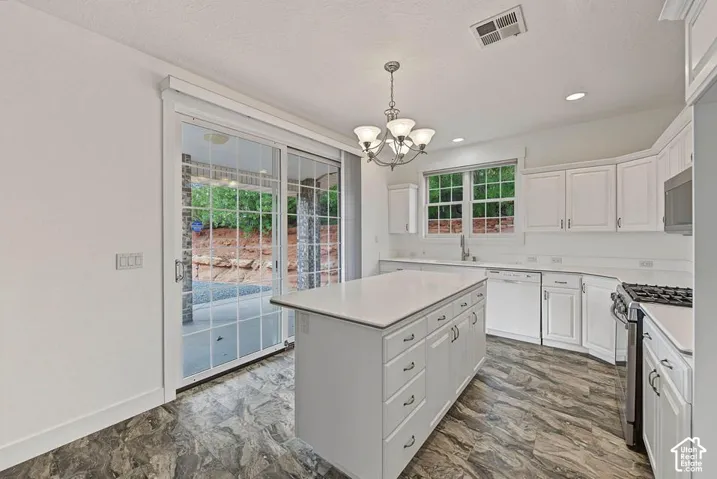 White kitchen featuring an island with drawers, white cabinetry, integrated stainless steel appliances, a gas range, and large sliding glass doors