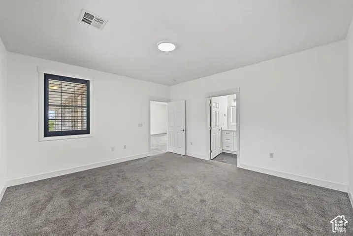 Spacious room with gray carpet, white walls, a single window with dark framing, and a flush-mount ceiling light