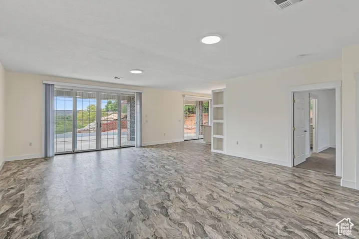 Spacious living area featuring wood-finish flooring, recessed lighting, built-in shelving, and multiple sliding glass doors opening to an exterior patio
