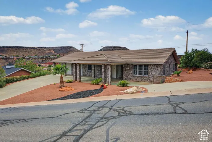 Stone-clad exterior with a tiled roof, covered entry, and xeriscaped front yard featuring a paved driveway and mature desert plantings