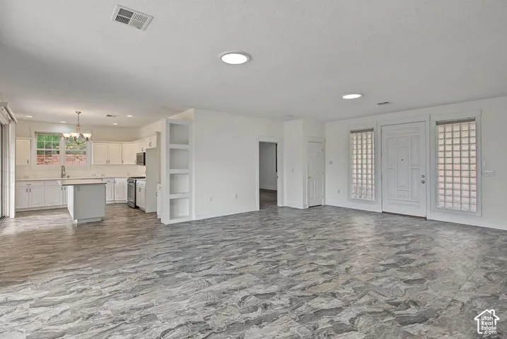 Spacious open-concept living area featuring stone-look tile flooring, recessed lighting, and a kitchen with white cabinetry and a center island