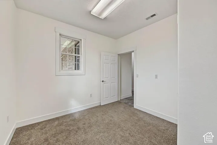 Neutral wall paint with carpet flooring, complemented by a single window with white trim