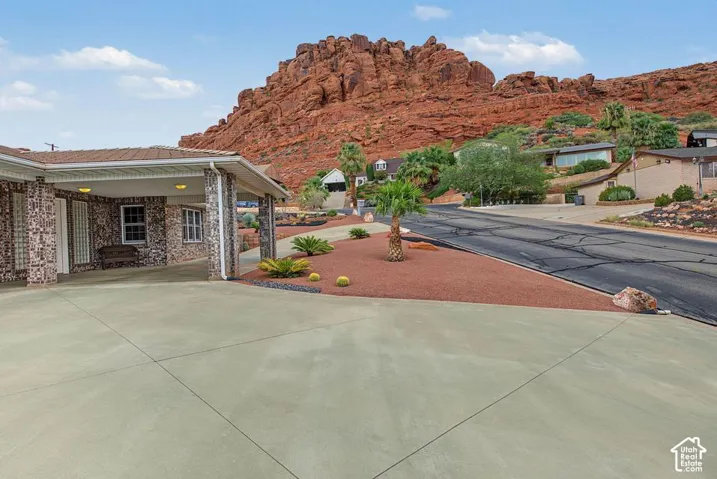 Exterior featuring brick facade, covered entry, concrete driveway, and desert landscaping