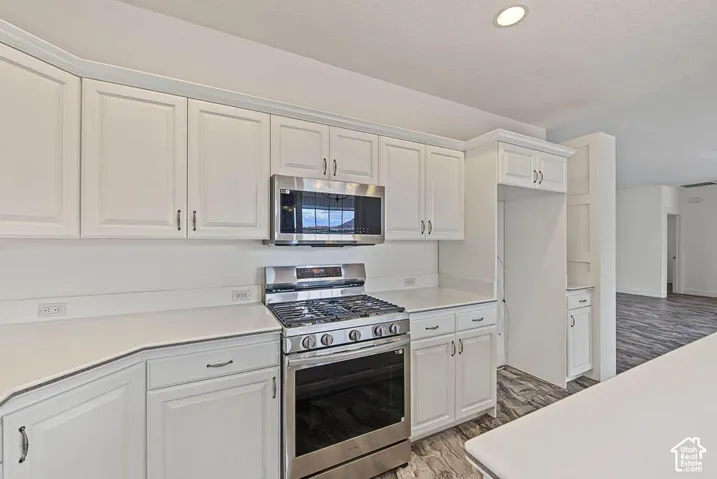 White cabinetry with brushed nickel hardware, stainless steel gas range, stainless steel microwave, light-toned countertops, and recessed ceiling lighting