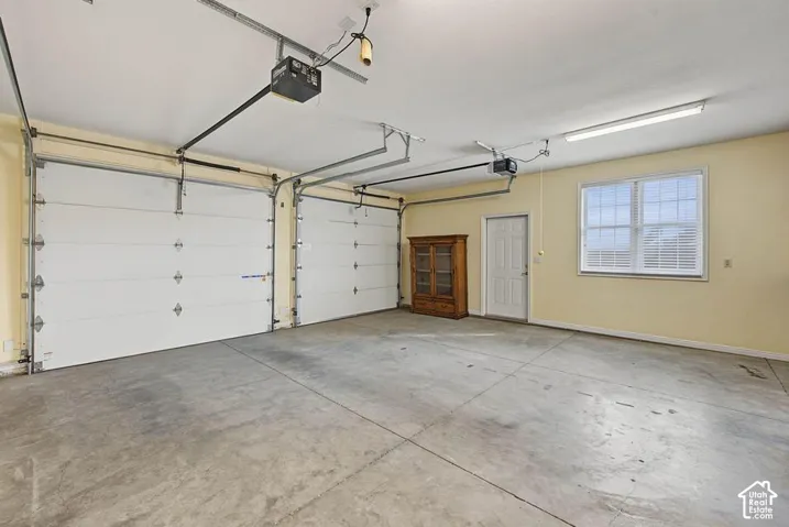 Two insulated garage doors with automatic openers, concrete flooring, exterior window with blinds, and white entry door