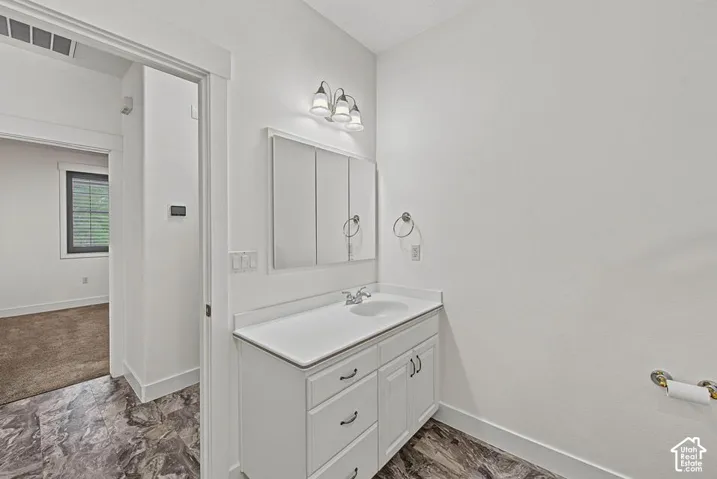 White vanity with integrated sink, modern light fixture, wall-mounted medicine cabinet, and patterned flooring