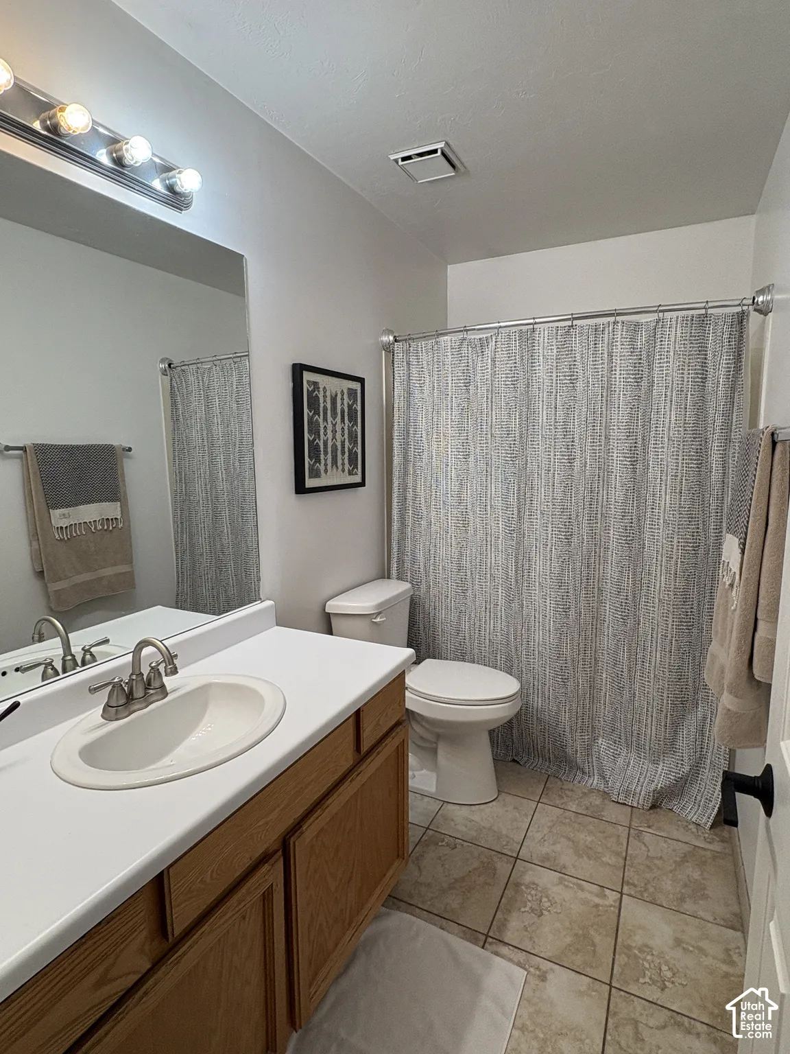 Bathroom featuring a wood-finish vanity with a white countertop, an integrated sink with a brushed nickel faucet, and a shower with a chrome rod