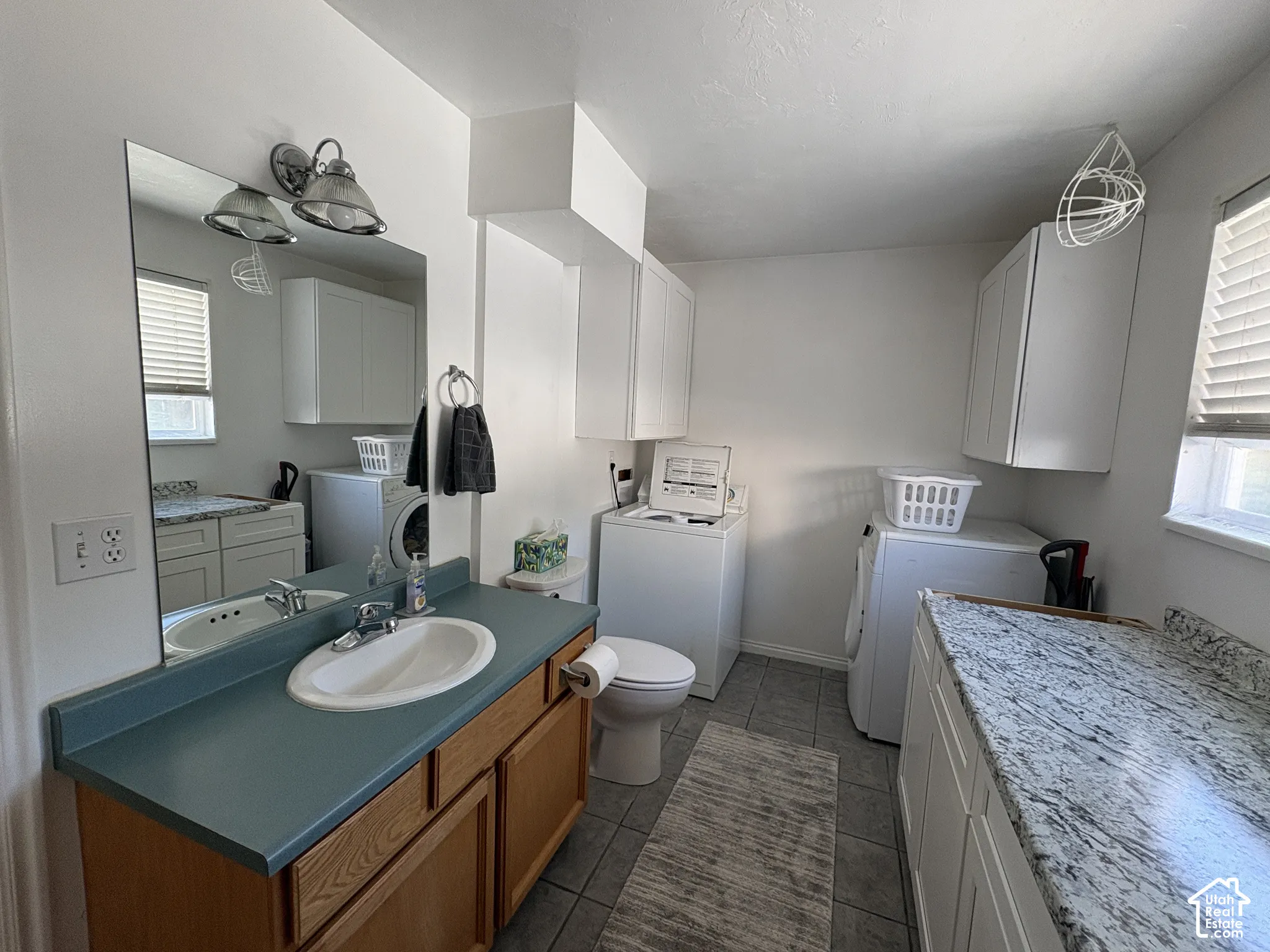 Integrated utility space featuring a vanity with a counter and sink, a toilet, a washer and dryer, and built-in white cabinetry