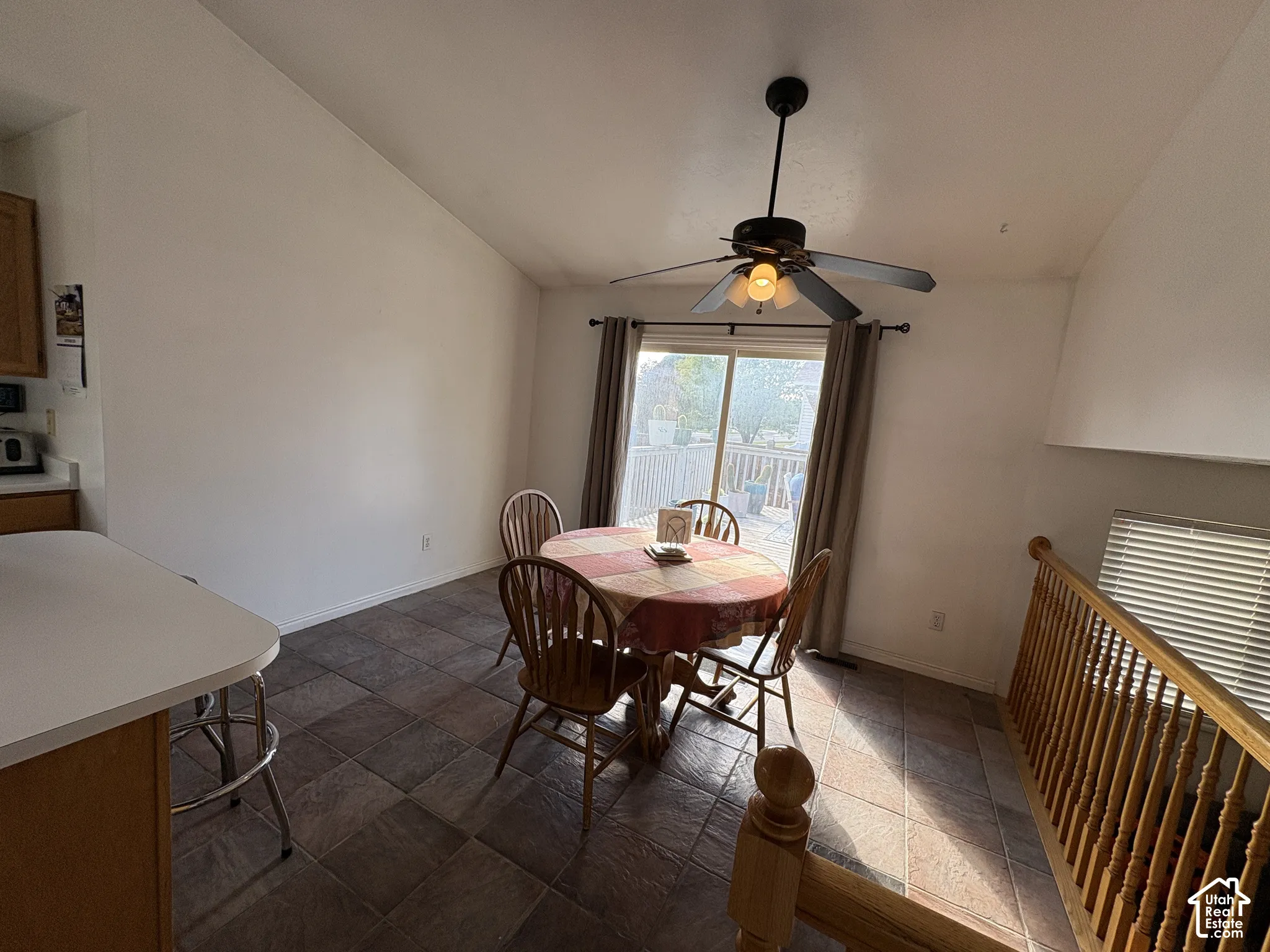 Vaulted ceiling, tiled flooring, built-in ceiling fan with light, sliding glass door, and staircase with railing