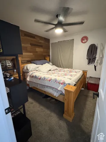 Secondary bedroom. Wood-finish accent wall, ceiling fan with integrated lighting, and neutral carpeting