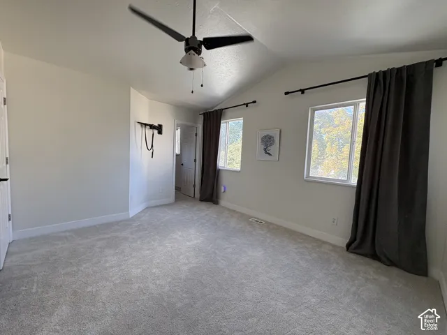 Vaulted ceiling with a ceiling fan, light-colored carpeting, multiple windows, and neutral wall tones