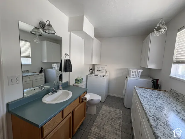 Integrated utility space featuring a vanity with a counter and sink, a toilet, a washer and dryer, and built-in white cabinetry