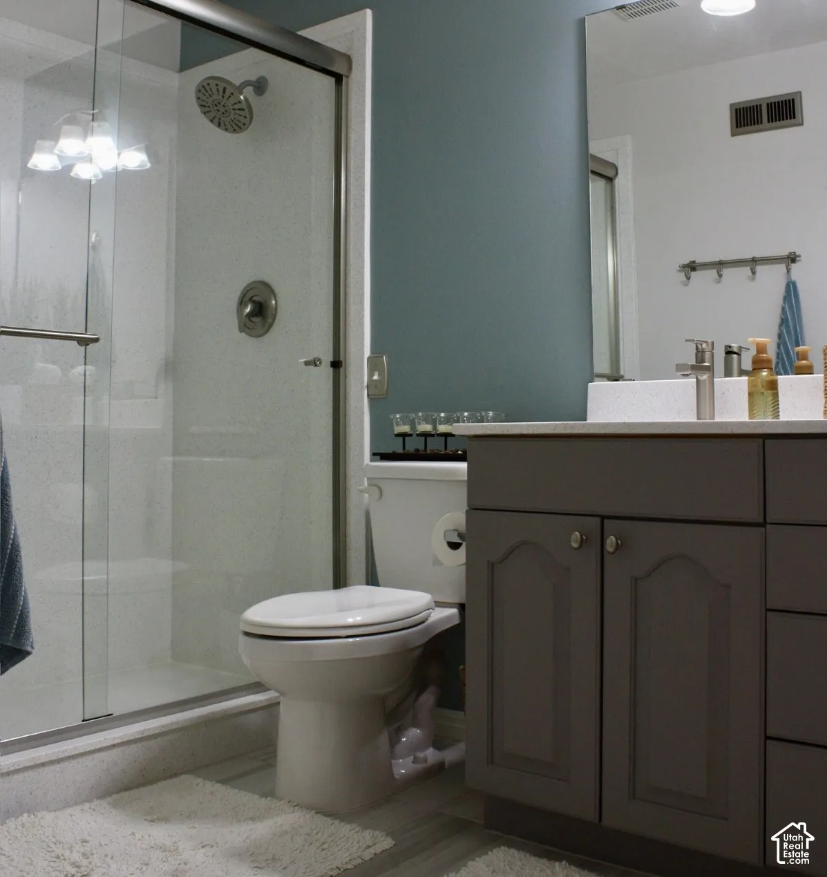 Glass-enclosed shower with a rainfall showerhead, single vanity with a white countertop, and a built-in cabinet