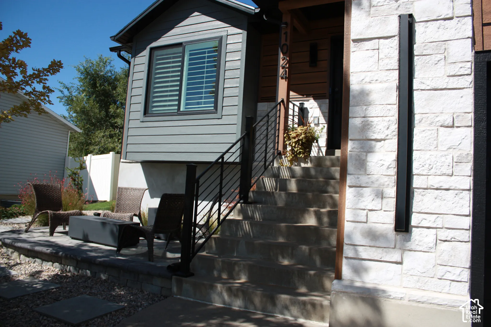 Stone facade, concrete steps with metal railing, wood-paneled entry, horizontal siding, and an exterior patio with retaining wall