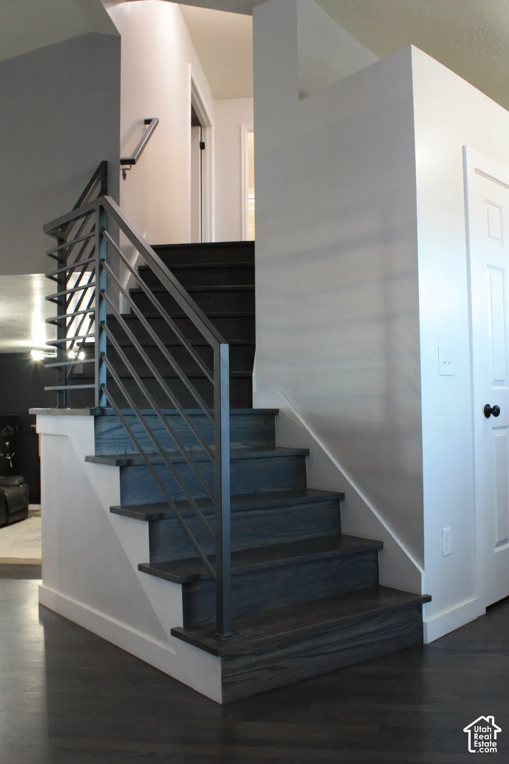 Modern staircase featuring wood-finish treads and risers, a contemporary metal railing, and white wall finishes