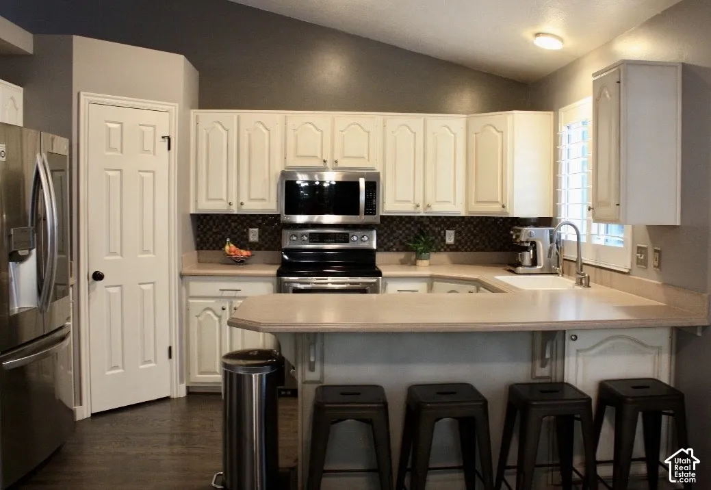 Kitchen featuring white cabinetry, stainless steel appliances, a tile backsplash, and wood-finish flooring
