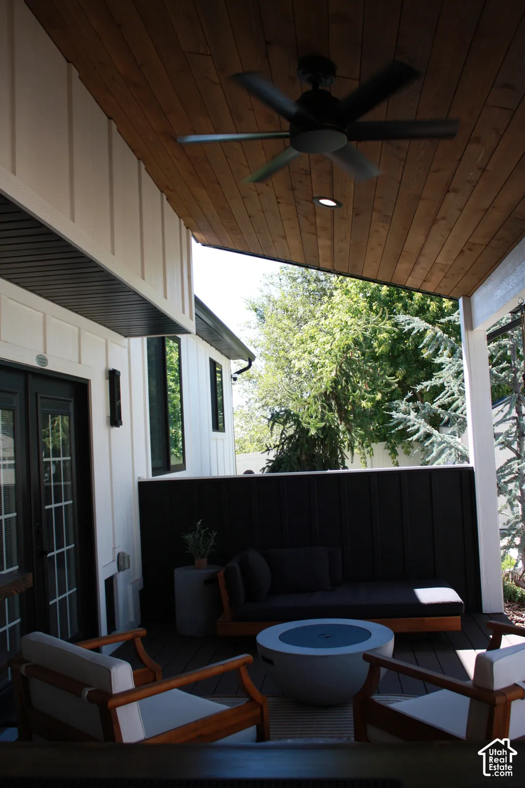 Covered patio with wood-finish ceiling, ceiling fan with integrated lighting, and black metal privacy screen