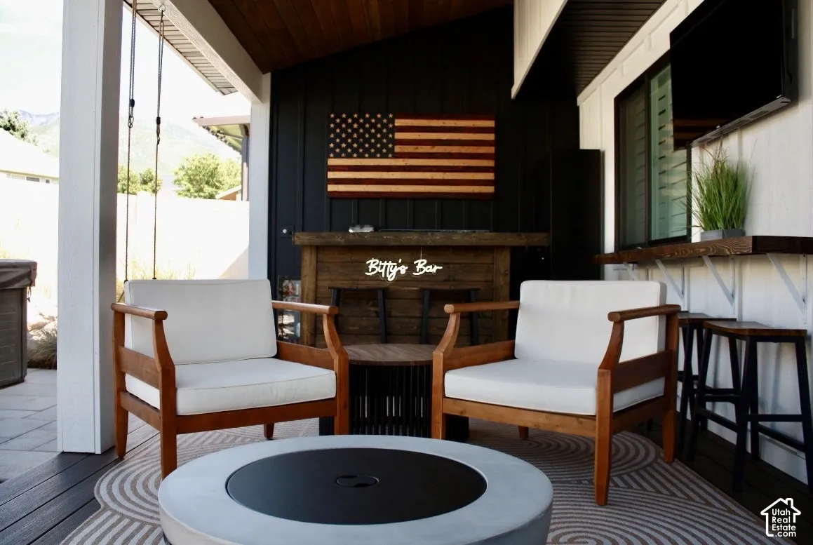 Covered outdoor patio featuring a slatted wood ceiling, a built-in bar area, and a concrete fire pit