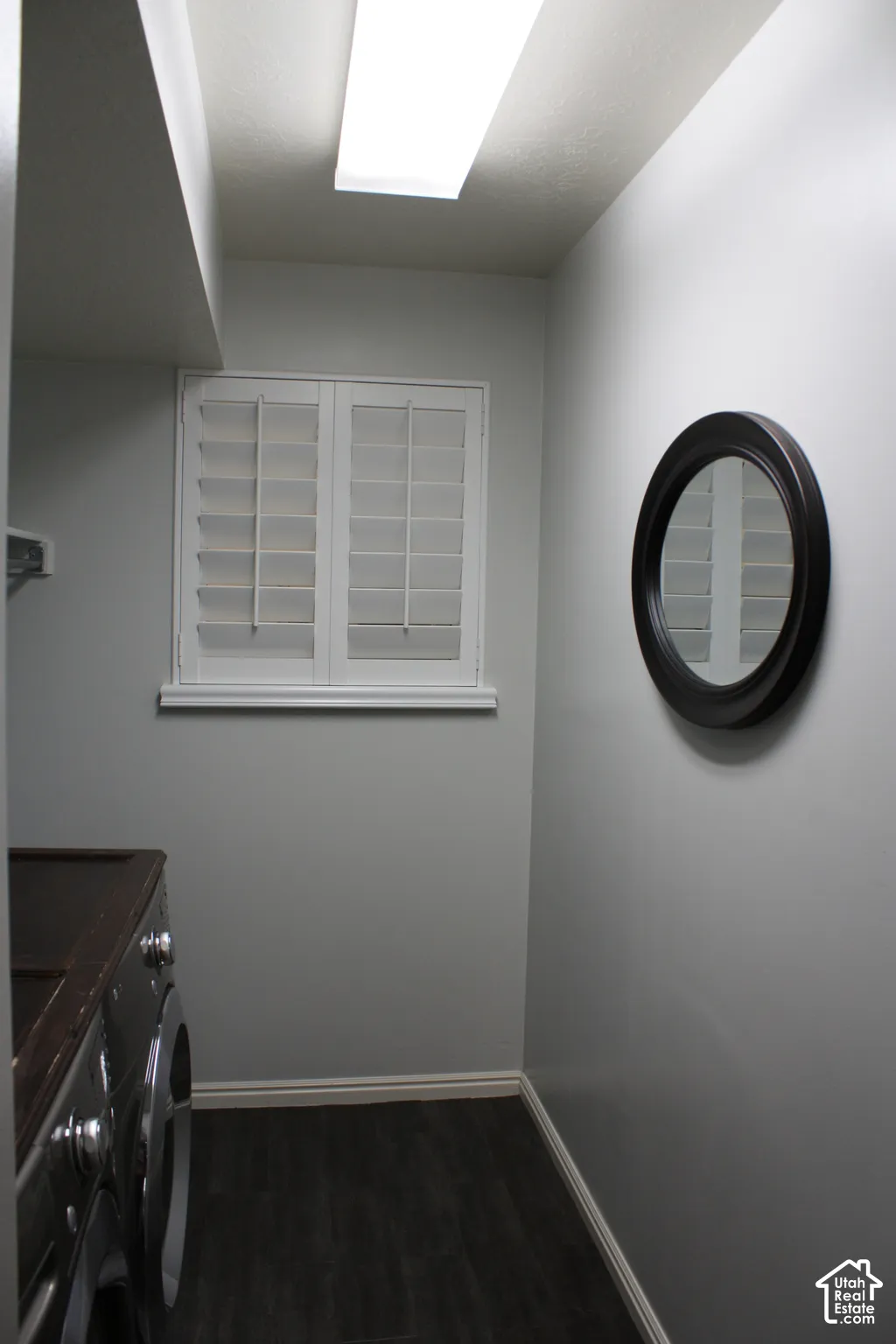 Window featuring white plantation shutters, overhead fluorescent lighting, and wood-finish flooring