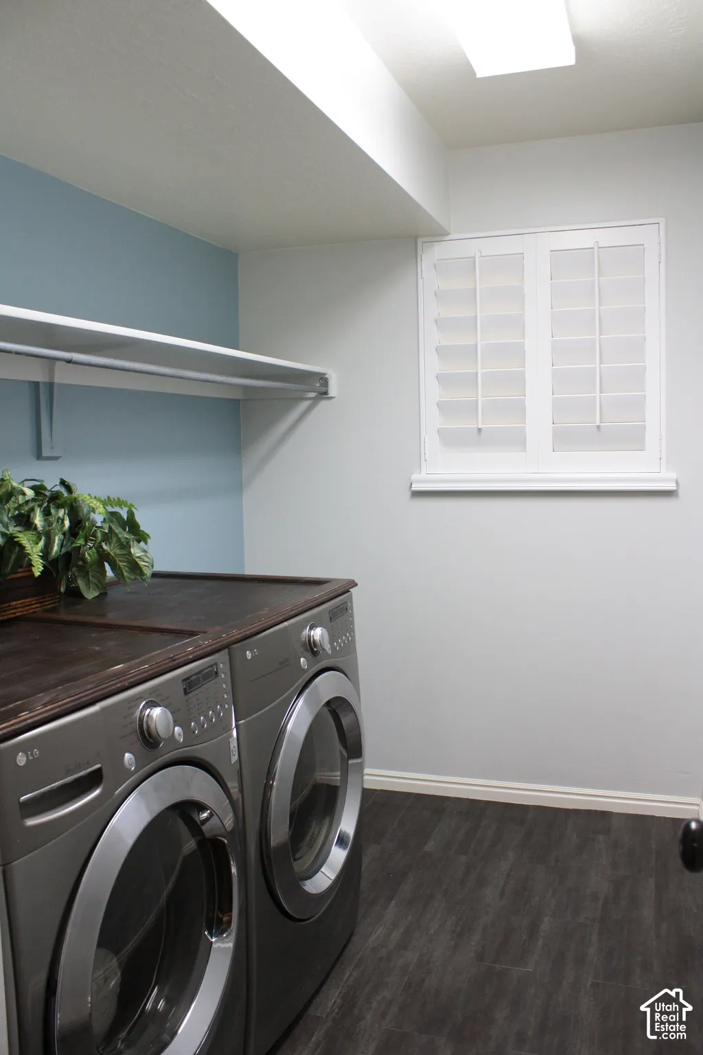 Utility space featuring dark wood-finish flooring, a white-framed window with plantation shutters, overhead lighting, and built-in shelving