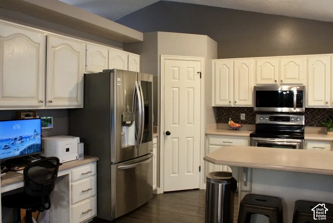 Kitchen featuring white cabinetry, stainless steel appliances, dark tile backsplash, and a built-in desk area