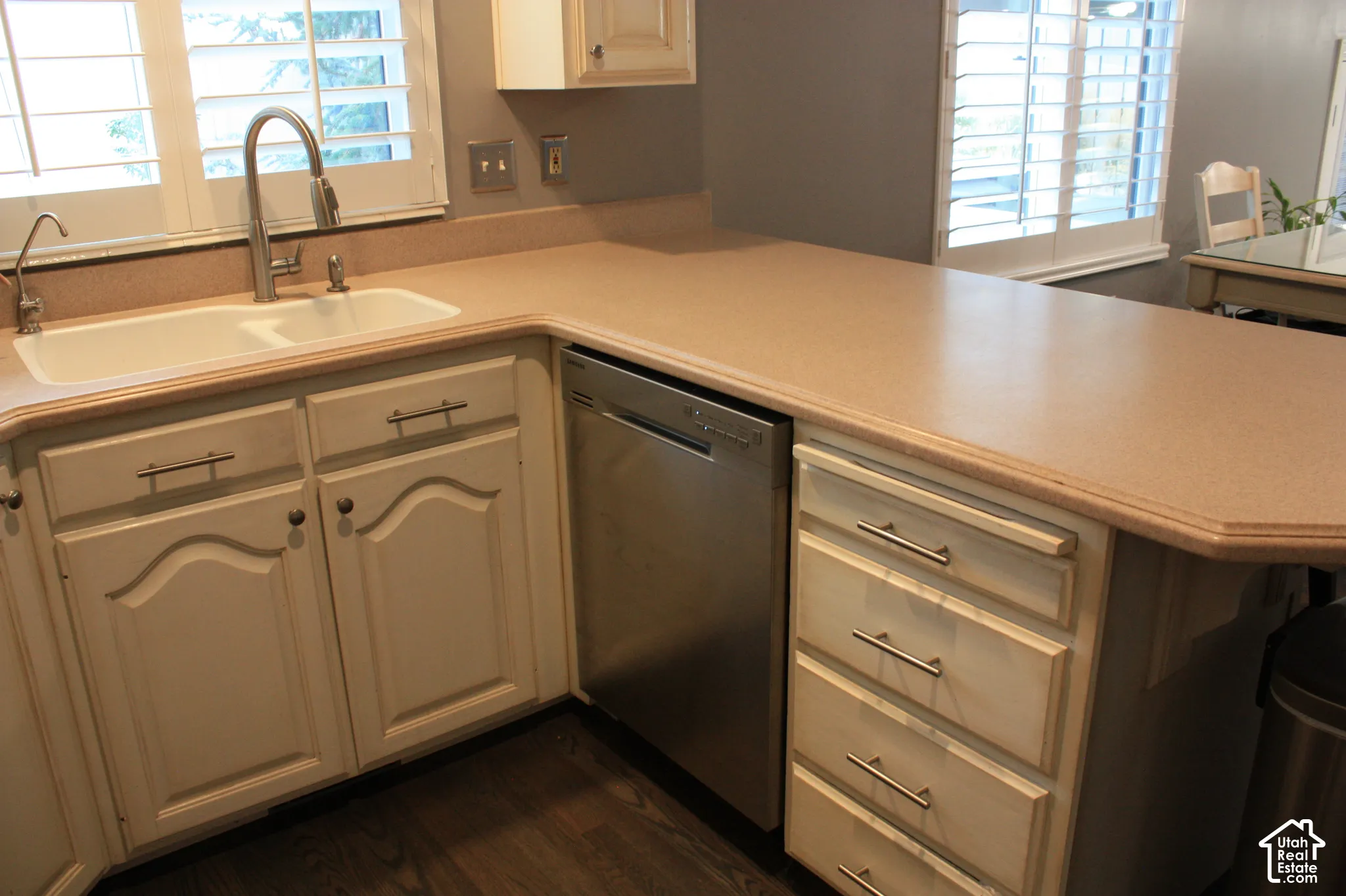 White double basin sink with gooseneck faucet, light-colored countertops, stainless steel dishwasher, and white cabinetry with brushed nickel hardware