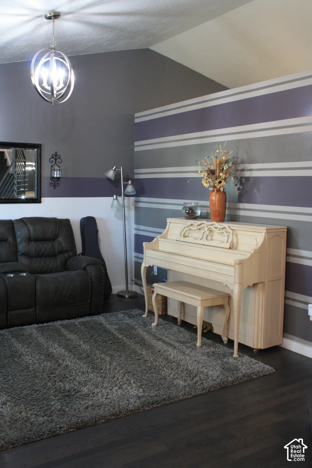 Vaulted ceiling with an orb pendant light fixture, dark wood-finish flooring, and accent wall with horizontal stripes