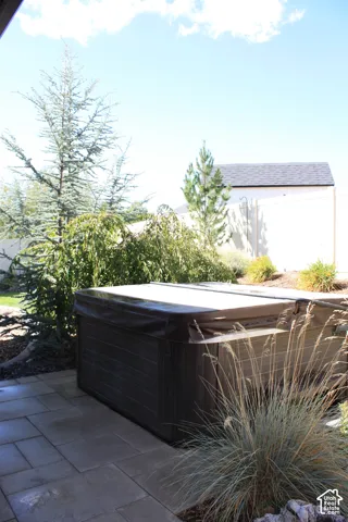 Paved patio area featuring a covered spa, surrounding evergreen trees, and integrated landscaping with ornamental grasses