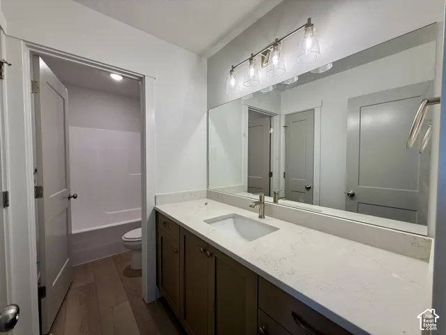Bathroom featuring a single vanity with a white countertop, an undermount sink, a wall-mounted mirror, and wood-finish flooring