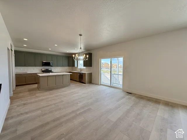 Open-concept living space with wood-finish flooring, a kitchen island, two-tone cabinetry, stainless steel appliances, and a sliding glass door with a balcony