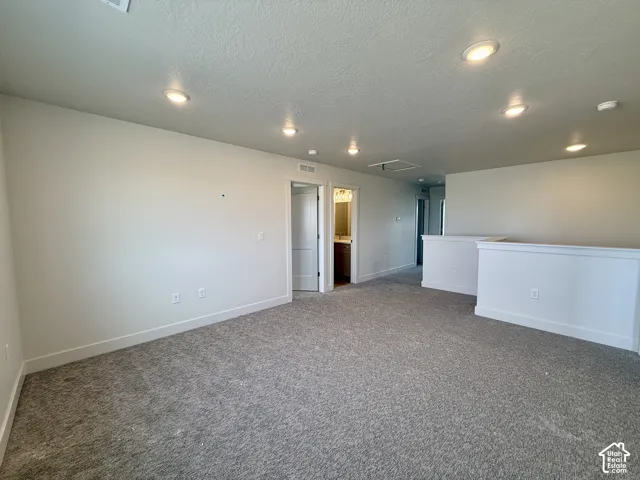 Spacious carpeted area with recessed lighting, white walls, and a half-wall partition