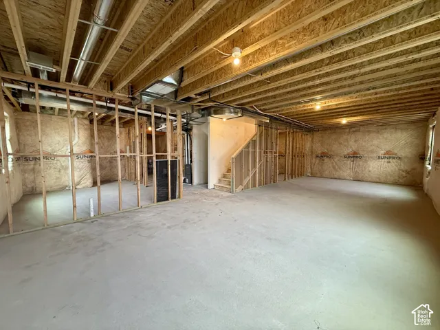 Unfinished basement featuring concrete flooring, exposed wood joists, framed interior walls, and a staircase