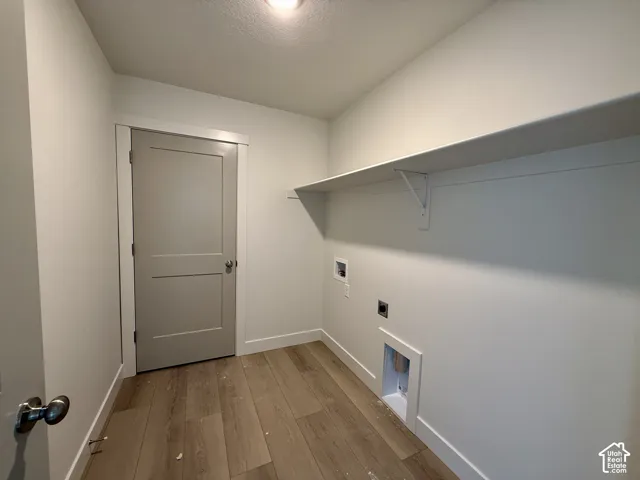 Wood-finish flooring, light grey interior door, white wall shelving, and utility hookups