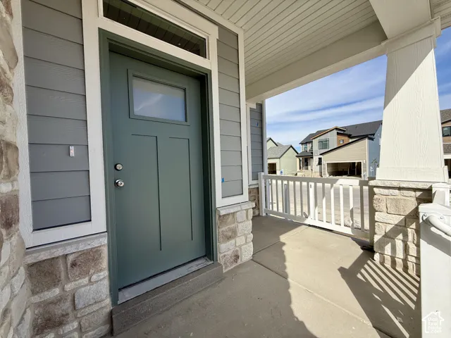 Covered concrete porch with stone veneer accents, gray horizontal siding, and a green entry door with a transom window