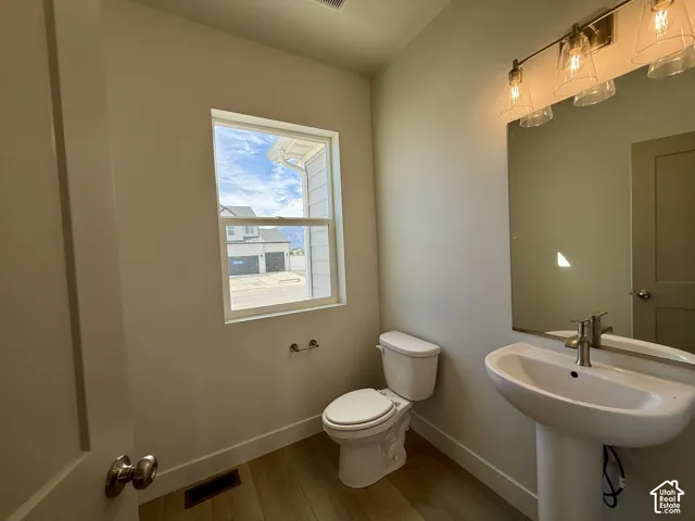 Pedestal sink with a polished chrome faucet, rectangular mirror, modern vanity lighting, and wood-finish flooring