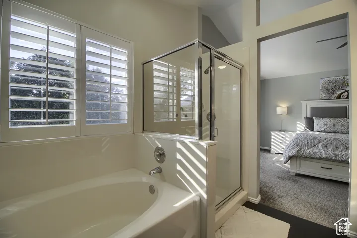 Built-in soaking tub, glass-enclosed shower, white window shutters, and vaulted ceiling
