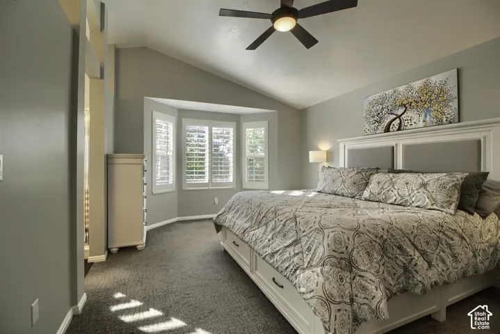 Vaulted ceiling, bay window with plantation shutters, ceiling fan with integrated lighting, and neutral carpeting